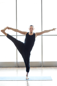 Serious handsome young yogis in black clothing balancing on one leg and holding toes in hand while , he doing extended hand-to-big-toe pose