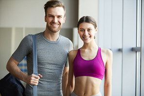 Happy confident young couple in good shapes visiting training together in fitness club, they smiling at camera