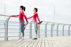 Full length portrait of two active  women stretching legs while jogging on pier outdoors , copy space