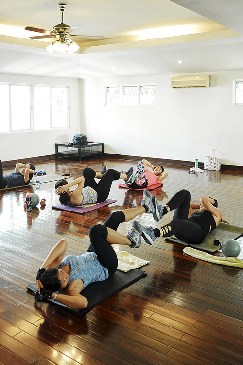 Vietnamese young women doing abs exercise in pairs during pilates class
