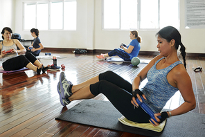 Fit young Asian women sitting on yoga mat and doing side twists with dumbbells