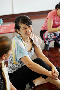 Pretty young smiling woman talking to friends after class in fitness studio