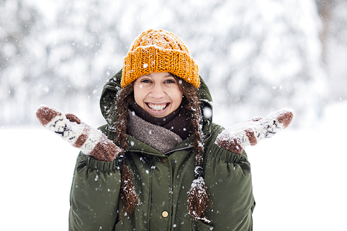 Waist up portrait of happy young woman enjoying snowfall in beautiful winter forest, copy space
