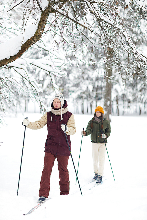 Full length portrait of active young couple skiing in beautiful winter forest, copy space
