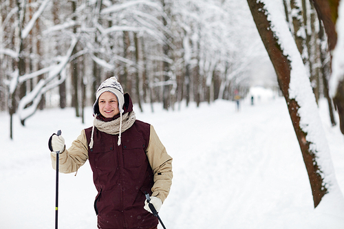 Waist up portrait of smiling young man skiing in forest enjoying winter and snow, copy space