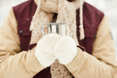 Close up of unrecognizable man holding cup of hot cocoa outdoors enjoying hike in winter, copy space