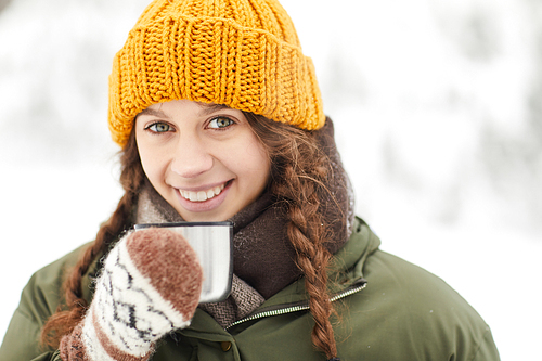 Head and shoulders portrait of pretty young woman drinking hot cocoa outdoors and  while enjoying winter hike, copy space