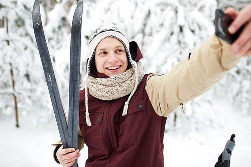 Waist up portrait of active young man taking selfie outdoors while skiing in winter forest