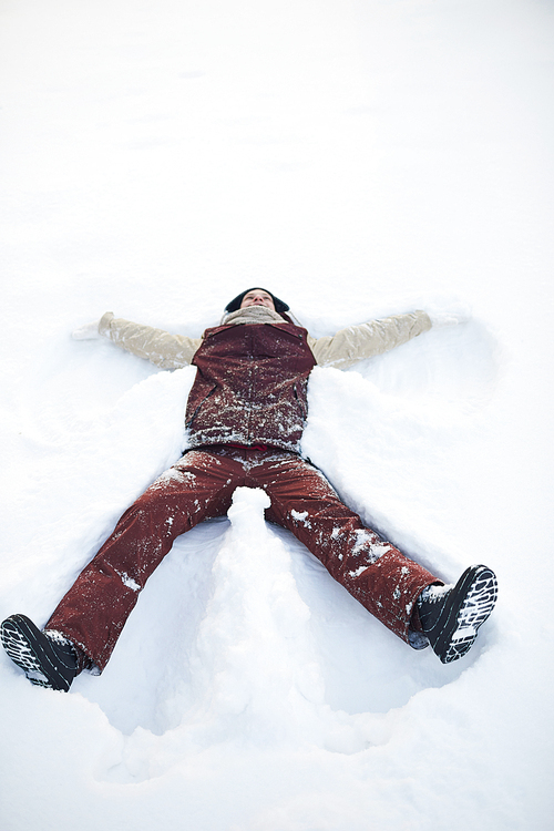 High angle portrait of happy young man lying in snow and making snow angels outdoors