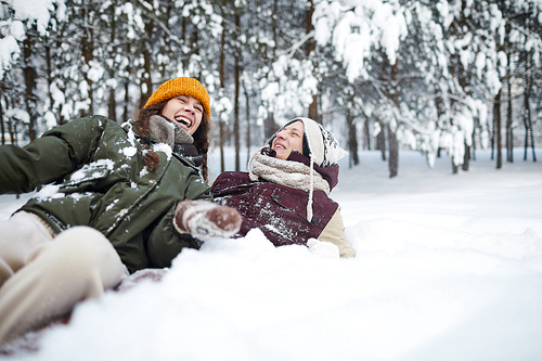 Portrait of playful young couple lying in snow while having fun outdoors in winter , copy space