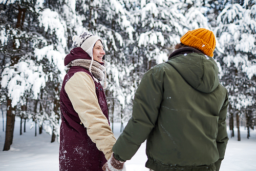 Back view portrait of loving couple holding hands while enjoying walk in beautiful winter forest, copy space