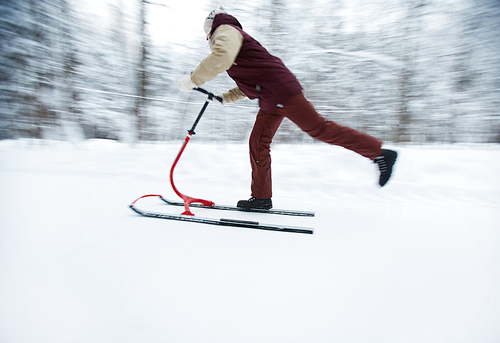 Side view portrait of active young man enjoying sleigh ride in winter forest sliding by past in blurred motion, copy space
