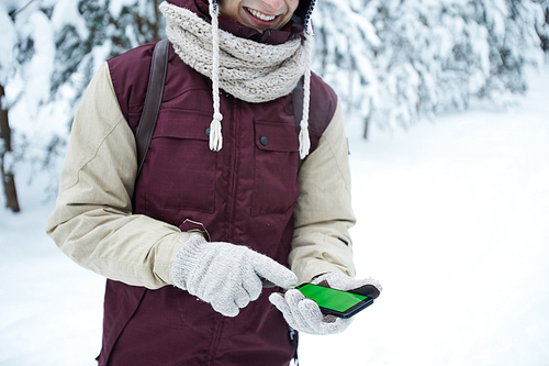 Mid section portrait of modern young man using smartphone during hike in winter forest, copy space