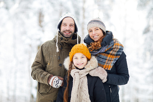Waist up portrait of happy modern family in winter forest posing with little girl and smiling at camera, copy space