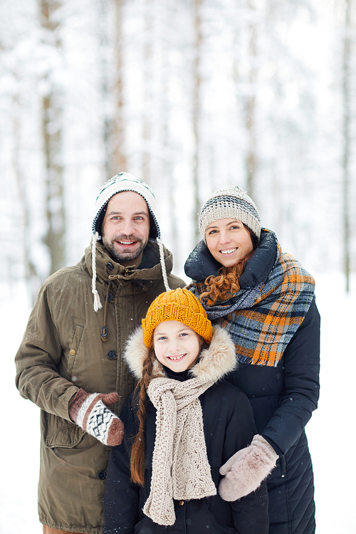Waist up portrait of happy modern family in winter forest posing with little girl and smiling at camera