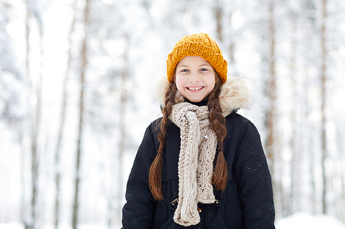 Waist up portrait of happy little girl in winter forest smiling at camera, copy space