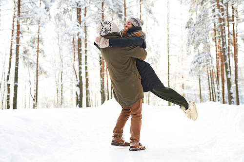 Full length portrait of playful couple embracing in winter forest and swirling around, copy space