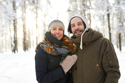 Waist up portrait of happy adult couple in winter forest  and smiling, copy space