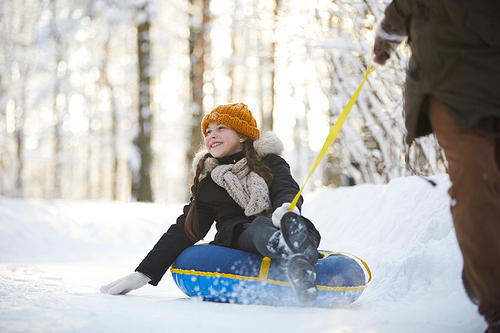 Full length portrait of happy little girl enjoying sleigh ride in beautiful winter forest, copy space
