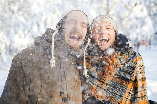 Waist up portrait of excited adult couple playing with snow in winter forest  and laughing
