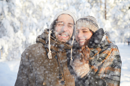 Waist up portrait of happy adult couple playing with snow in winter forest  and smiling, copy space
