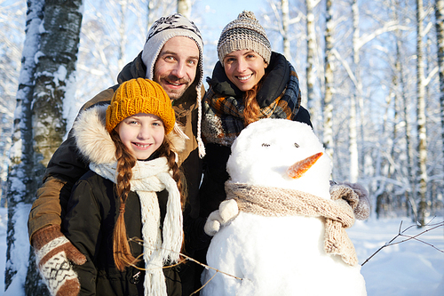 Waist up portrait of happy family building snowman in winter forest and smiling at camera, copy space