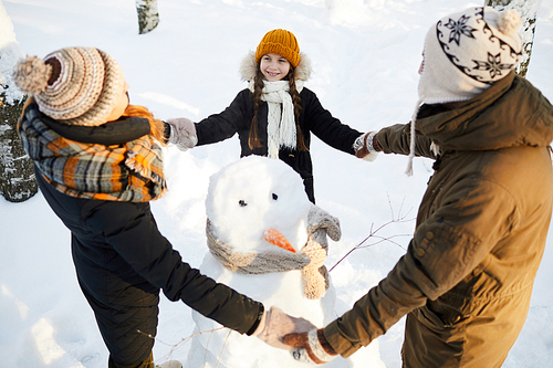High angle portrait of happy family building snowman in winter forest and laughing, copy space