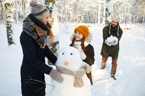 Portrait of happy family building snowman in winter forest and having fun, copy space