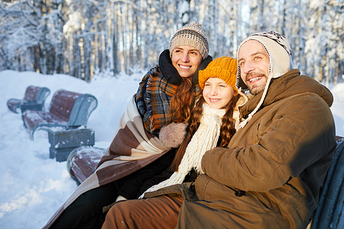 Portrait of happy family sitting on bench in beautiful winter forest posing together and looking away, copy space