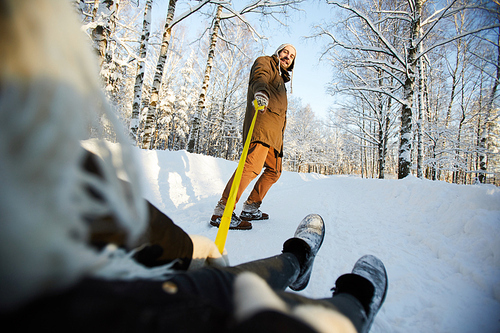 Low angle portrait of happy adult man tugging sleigh in beautiful winter park, copy space