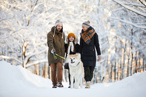 Full length portrait of happy family enjoying walk with dog in winter forest, copy space