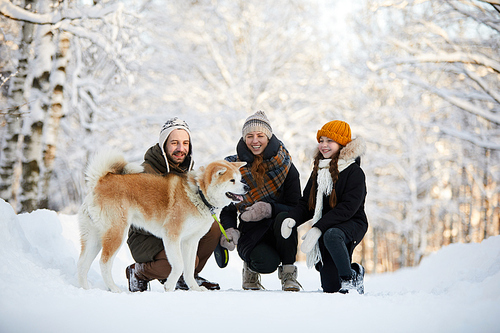 Full length portrait of happy family enjoying walk with dog in beautiful winter park, copy space