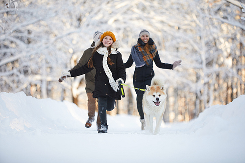 Full length portrait of happy girl walking dog in beautiful winter park, copy space