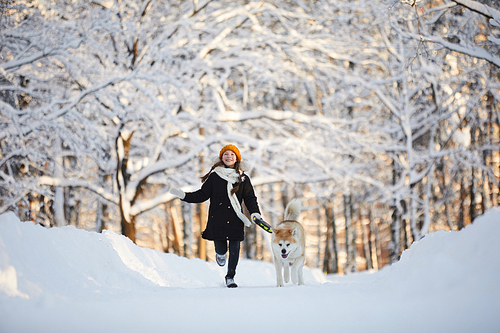 Full length portrait of happy little girl walking dog in beautiful winter park, copy space