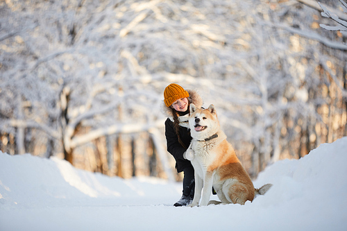 Full length portrait of happy girl posing with dog in beautiful winter park, copy space