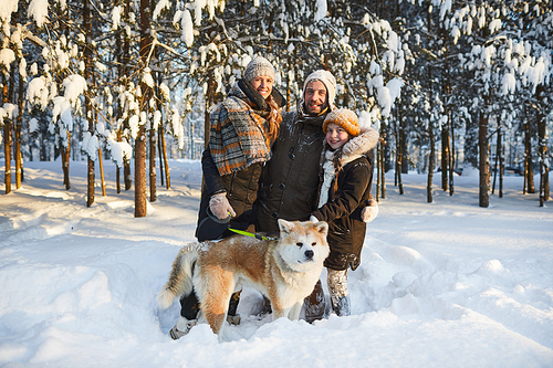 Portrait of happy family enjoying walk with dog in beautiful winter park and , copy space