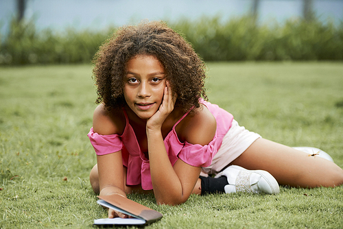 content relaxed african teenage girl in pink casual blouse lying on green grass outdoors and leaning head on hand while , she viewing notes in 다이어리