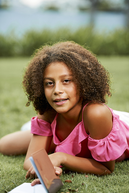 smiling attractive african-american teen girl with afro hairstyle lying on grass and , she writing 다이어리