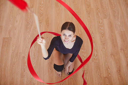 Directly above view of positive ambitious attractive female rhythmic dancer twirling gymnastic ribbon and 