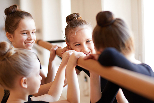 Group of cute little girls standing at bar and chatting cheerfully during ballet class, copy space