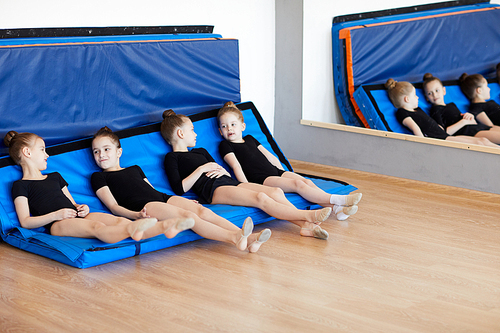 Group of little girls relaxing laying on mats after dance practice in studio, copy space