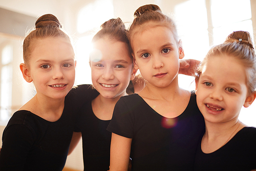 Group of little girls posing together during dance or gymnastics practice in studio lit by sunlight, copy space