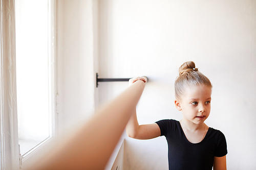 High angle portrait of cute little girl standing by bar in dance class and looking away,