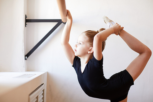Side view portrait of cute little girl standing by bar in ballet class  during practice, copy space