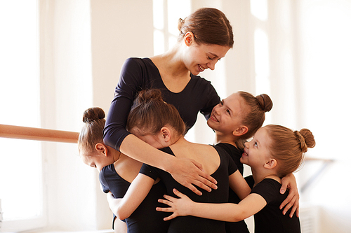 Group of little girls hugging ballet teacher in studio lit by warm sunlight, copy space