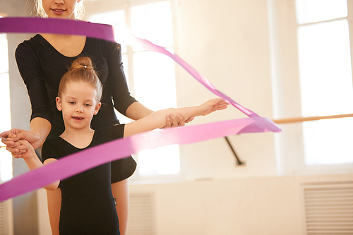 Little girl doing gymnastics moves with ribbon in studio lit by warm sunlight, copy space