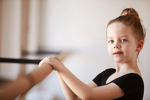 Portrait of cute little girl in ballet class  while posing by bar, copy space