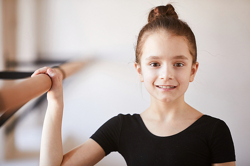Portrait of little girl in ballet class  while posing by bar, copy space