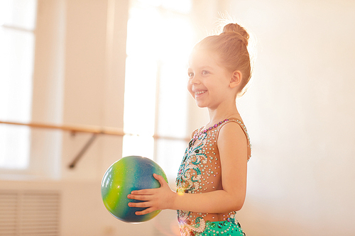Side view portriat of little gymnast posing holding ball in sunlight, copy space