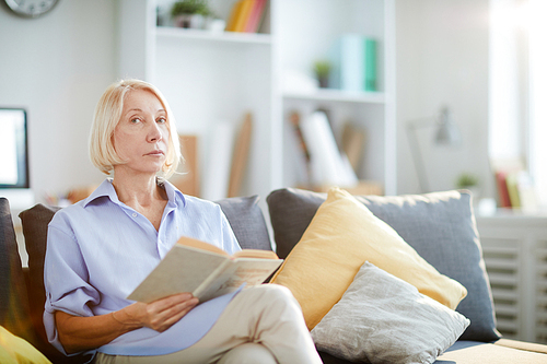 Portrait of contemporary adult woman reading book sitting on sofa at home and , copy space